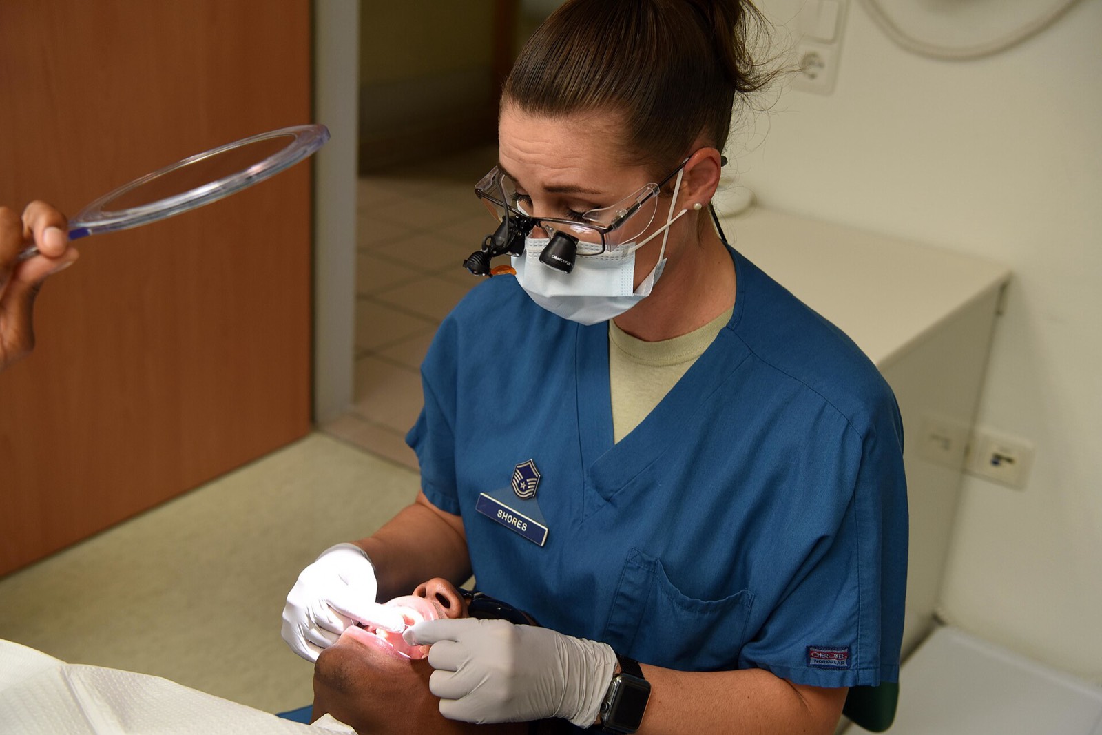 A dentist wearing loupes treating an adult patient